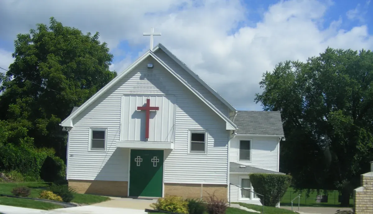 A white frame church with a red cross and green doors on a raised basement, Merrimac, 2009